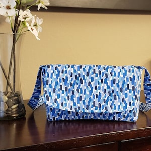 Może przedstawiać: Niebieska i biała wzorzysta torba listonoszka z klapką i regulowanym paskiem.