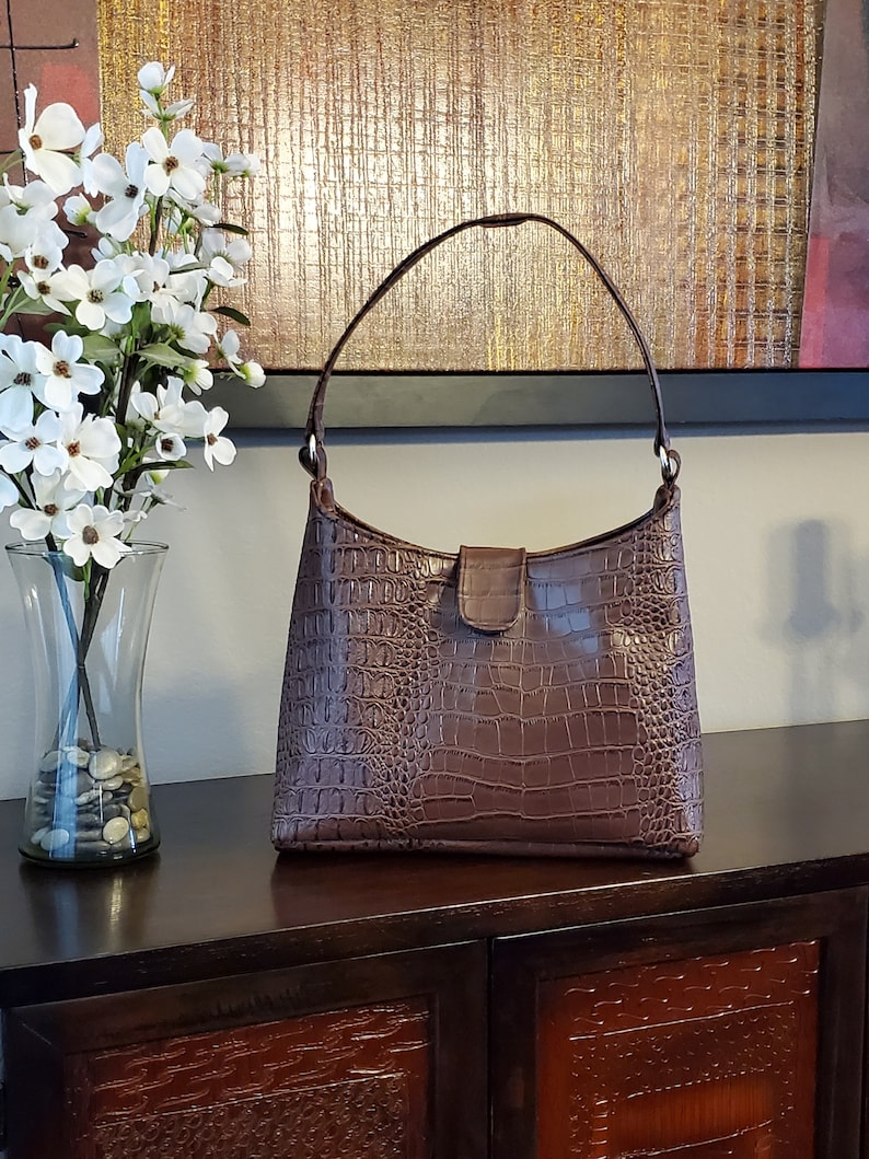 May include: A brown crocodile-embossed leather handbag with a single top handle and a flap closure.