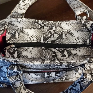 May include: A black and white snakeskin print handbag with a zipper closure and two silver rings on the handles. The bag has a red lining.
