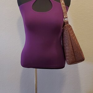 May include: A purple halter top with a keyhole cutout on a black mannequin with a brown crocodile-embossed handbag.