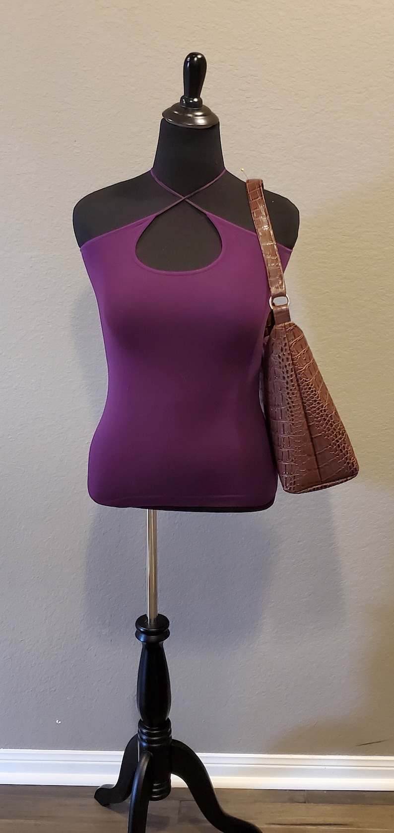 May include: A purple halter top with a keyhole cutout on a black mannequin with a brown crocodile-embossed handbag.