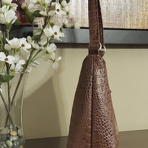 May include: A brown leather handbag with a crocodile-embossed pattern. The bag has a single top handle and a flap closure.
