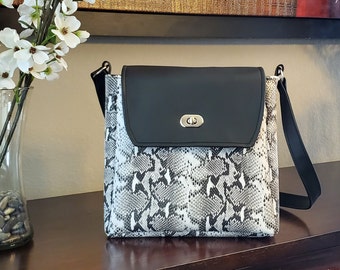 May include: A black and white snakeskin patterned crossbody bag with a black flap and silver hardware. The bag has a long adjustable strap.