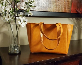 May include: A brown leather tote bag with two straps. The bag is sitting on a wooden table.