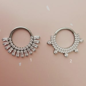 May include: Two silver hoop earrings with clear crystal embellishments. The first earring has a row of rectangular crystals and the second earring has a row of round crystals with a pointed design.