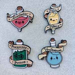 Puede incluir: Cuatro pines de esmalte con diseños de botellas de pociones. Los pines incluyen Amortentia, Felix Felicis, Polyjuice Potion y Veritaserum. Cada botella tiene un color y una expresión únicos, con texto en una pancarta.