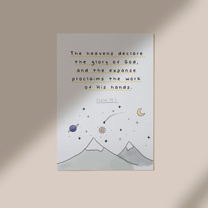 Op de afbeelding: Een witte kaart met een handgetekend ontwerp van bergen, sterren, een zon, een maan en een planeet. De tekst op de kaart luidt "De hemel verkondigt de heerlijkheid van God, en de uitgestrektheid verkondigt het werk van zijn handen. Psalm 19:1".
