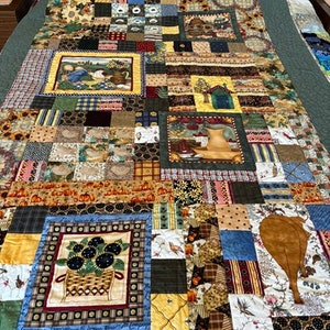 May include: A patchwork quilt featuring a mix of floral, geometric and plaid patterns in a variety of colours, including brown, green, yellow and blue. The quilt is made up of many different squares and rectangles, and is a beautiful example of handmade craftsmanship.
