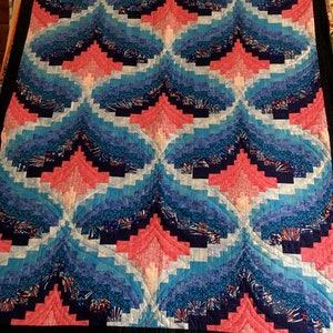 May include: A quilt with a log cabin pattern in shades of blue, pink, and white. The quilt is made of fabric with a variety of patterns, including stars, stripes, and polka dots.
