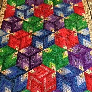 May include: A quilt featuring a geometric pattern of cubes in shades of red, green, blue, and purple. The cubes are arranged in a repeating pattern, creating a three-dimensional effect.