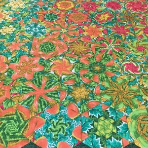 May include: A colourful quilt with a geometric pattern of green, orange and red. The quilt is made up of many smaller squares, each with a different design. The quilt is a beautiful example of patchwork quilting.