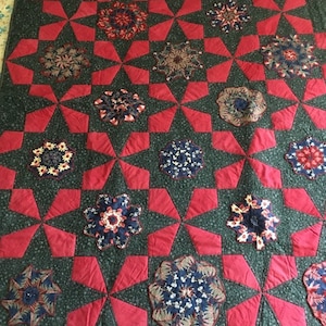 May include: A quilt with a green background and red star-shaped patches. Each star patch has a circular, multi-coloured design in the centre.