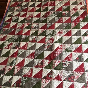 May include: A quilt made of red, green and white fabric with a geometric pattern of triangles. The quilt is made of patchwork fabric and has a rustic, vintage look.