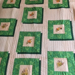May include: A quilt with a green and white leaf pattern. The quilt is made up of squares with a green border and a white centre. The leaves are embroidered in the centre of each square.