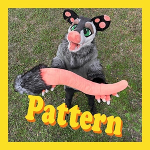 May include: A full-body opossum costume featuring a gray and black faux fur head with large ears, green eyes, and a pink nose. The costume includes a long, segmented pink tail and matching pink paws with white claws. The word Pattern is visible.