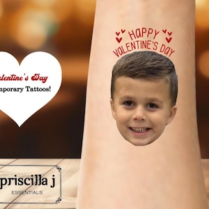 May include: A Valentine's Day temporary tattoo featuring a smiling child's face with the words "Happy Valentine's Day" above. A white heart with the text "Valentine's Day Temporary Tattoos!" is also visible.