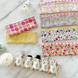 May include: A set of six fabric pouches with floral and geometric patterns. The pouches are lined up in a row on a white marble surface. The pouches are ideal for storing small items such as jewellery, makeup, or essential oils.
