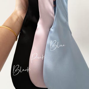 May include: Three satin bags in black, pink, and blue are held up against a white background. The word "Black" is written in cursive on the black bag, "Pink" on the pink bag, and "Blue" on the blue bag.