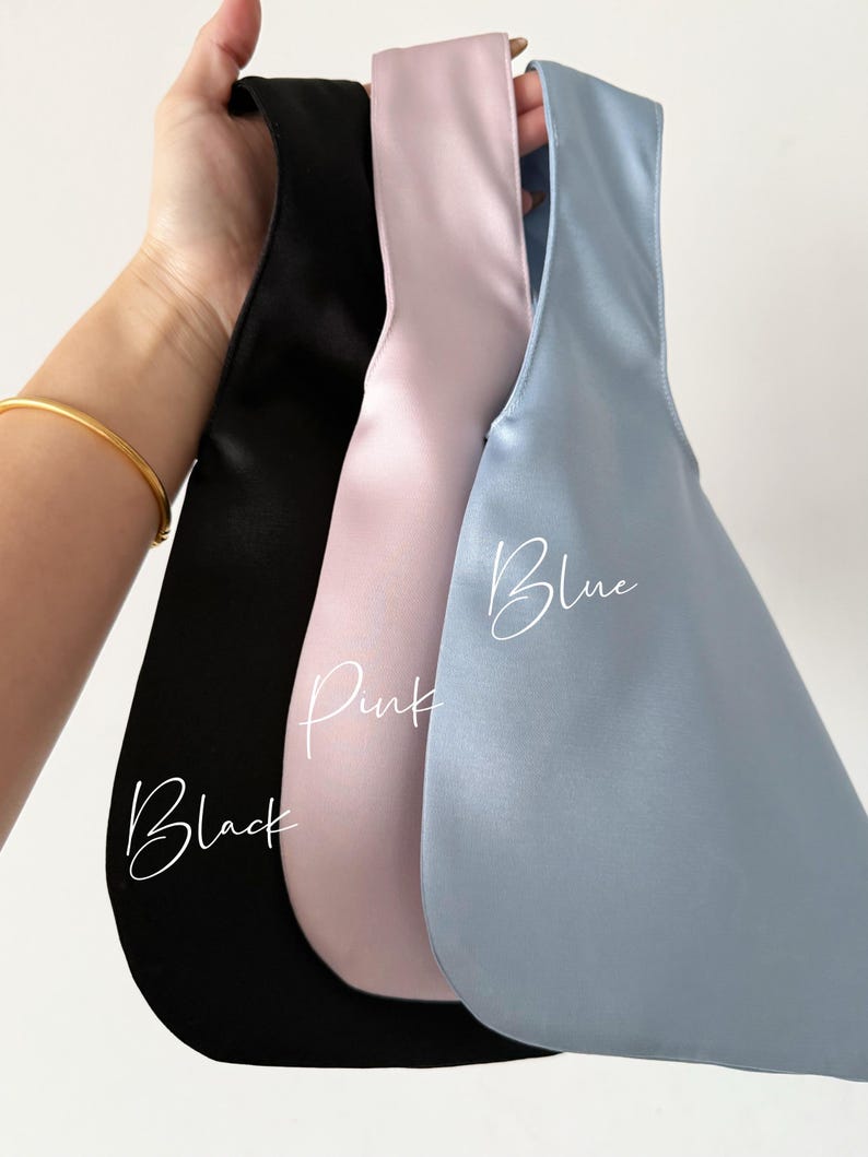May include: Three satin bags in black, pink, and blue are held up against a white background. The word "Black" is written in cursive on the black bag, "Pink" on the pink bag, and "Blue" on the blue bag.