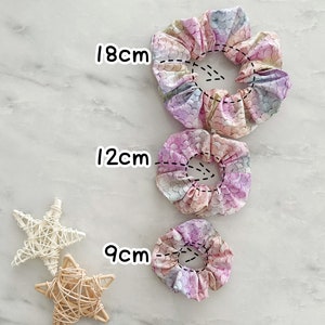 K&ouml;nnte beinhalten: Drei bunte Haargummis mit einem Meerjungfrauen-Schuppenmuster. Die Haargummis haben einen Durchmesser von 9 cm, 12 cm und 18 cm.