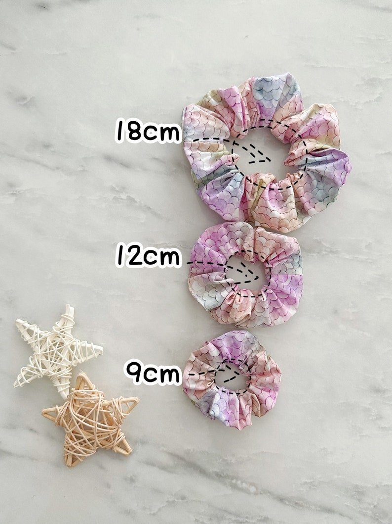 K&ouml;nnte beinhalten: Drei bunte Haargummis mit einem Meerjungfrauen-Schuppenmuster. Die Haargummis haben einen Durchmesser von 9 cm, 12 cm und 18 cm.