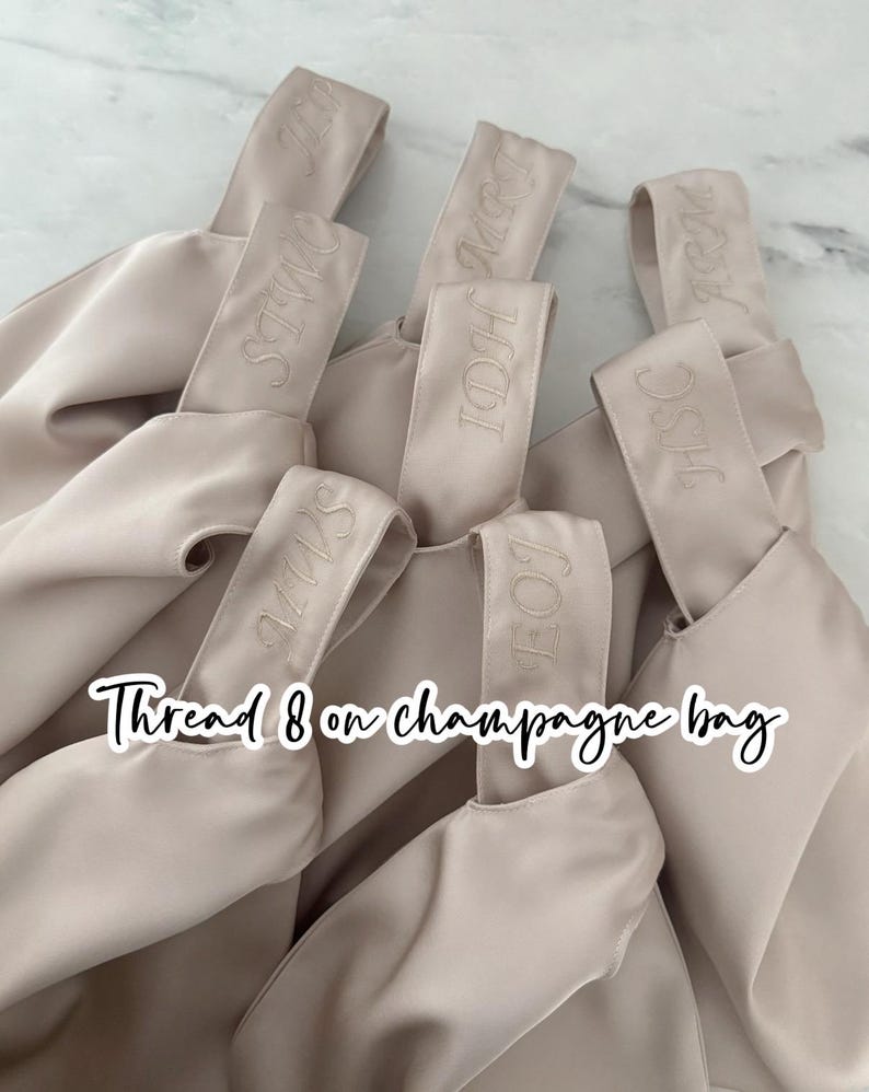 May include: A collection of beige satin champagne bags, each with a handle embroidered with initials. The bags are arranged in a close-up shot, with the text "Thread 8 on champagne bag" overlaid on the image.