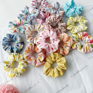 K&ouml;nnte beinhalten: Eine Sammlung von 15 bunten Stoffscrunchies mit Blumen- und anderen Mustern. Die Scrunchies sind auf einer wei&szlig;en Oberfl&auml;che zu einem Stapel angeordnet. Die Scrunchies sind handgefertigt und haben eine Vielzahl von Farben und Mustern.