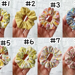 K&ouml;nnte beinhalten: Acht handgefertigte Scrunchies in verschiedenen Blumenmustern. Die Scrunchies sind aus Stoff und haben einen gerafften Look. Die Scrunchies sind in zwei Reihen zu je vier angeordnet, wobei jedes Scrunchie von 1 bis 8 nummeriert ist.