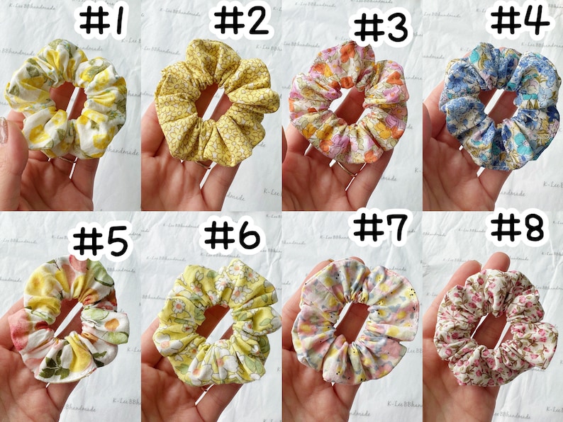 K&ouml;nnte beinhalten: Acht handgefertigte Scrunchies in verschiedenen Blumenmustern. Die Scrunchies sind aus Stoff und haben einen gerafften Look. Die Scrunchies sind in zwei Reihen zu je vier angeordnet, wobei jedes Scrunchie von 1 bis 8 nummeriert ist.