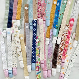 May include: A collection of colourful fabric dummy clips with various patterns, including polka dots, stripes and floral designs. The clips are attached to white plastic clips.