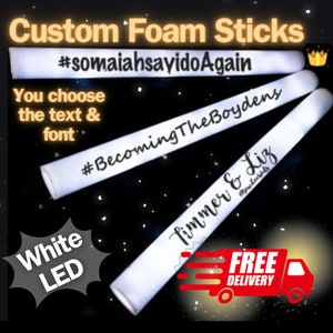 May include: Two white foam sticks with black text. The text on the top stick reads "#somaiahsayidoAgain #BecomingTheBoydens". The text on the bottom stick reads "Timmer & Liz #newlifebits".