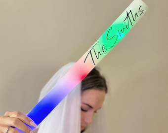 May include: A glowing LED light stick with a gradient of colors, from blue to red, and the text "The Smiths" in cursive. The stick is held by a person wearing a veil.