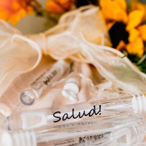 May include: A close-up of a clear plastic tube with a white wand inside. The tube is labeled "Salud!" and is surrounded by a white ribbon and orange flowers.