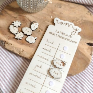 Peut inclure: Tableau de comportement en bois avec le nom "Romy" en haut. Le tableau porte l'inscription "La Météo de mon Comportement" et les jours de la semaine. Comprend des aimants en bois en forme de nuage et de soleil.