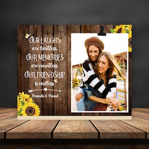 Può includere: Un cartello di legno con una foto di due donne che sorridono. Il cartello ha un design a girasole e il testo "OUR LAUGHS are limitless OUR MEMORIES are countless OUR FRIENDSHIP is endless Brandie & Friend".