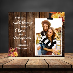May include: A wood-grain background with a white quote that reads "I can do all things through Christ who strengthens me - Philippians 4:13". A photo of two women smiling and hugging is in the centre of the image.