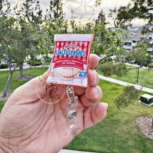 May include: A red and white Uncrustables peanut butter and strawberry jam sandwich keychain with a clear plastic badge holder.
