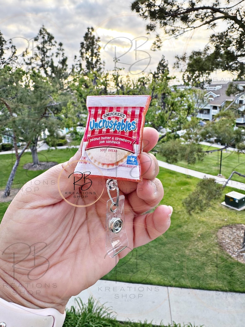 May include: A red and white Uncrustables peanut butter and strawberry jam sandwich keychain with a clear plastic badge holder.