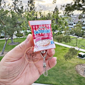 May include: A red and white Uncrustables peanut butter and strawberry jam sandwich keychain. The keychain features the Smucker's logo and the text "Uncrustables" in white letters. The keychain is attached to a silver metal clip.