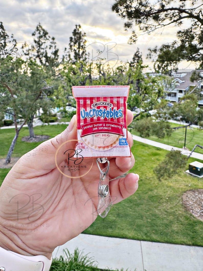 May include: A red and white Uncrustables peanut butter and strawberry jam sandwich keychain. The keychain is made to look like a real Uncrustables package.