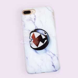 May include: White marble iPhone case with a black and red Pac-Man character graphic.