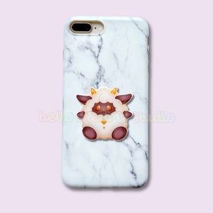 Op de afbeelding: Witte marmeren telefoonhoesje met een cartoon schaap ontwerp. Het schaap heeft een pluizig wit lichaam, bruin gezicht en poten, en kleine gele hoorns. De tekst "hello cherry studio" is aanwezig.