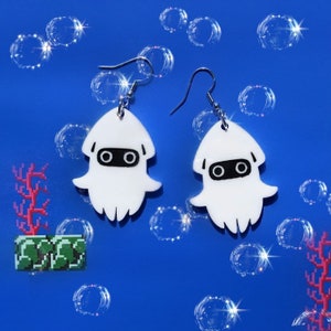 May include: A pair of white squid earrings with black eyes and silver hooks. The earrings are on a blue background with white bubbles.