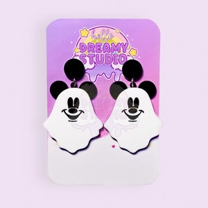 May include: A pair of white ghost earrings with black Mickey Mouse ears and a smiling face. The earrings are on a card with the text "hello DREAMY STUDIO".