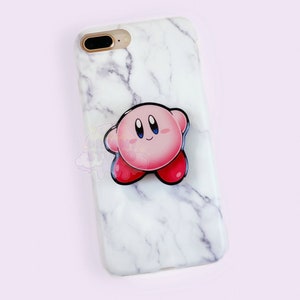 Könnte beinhalten: Eine weiße Marmor-iPhone-Hülle mit einem pinkfarbenen und roten Kirby-Charakter-Handyhalter.