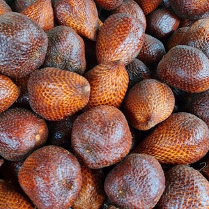 May include: A collection of salak fruits, also known as snake fruit, featuring a distinct reddish-brown, scaly, and textured skin. Each fruit has a teardrop or oval shape with a firm, overlapping pattern that covers the entire exterior surface.