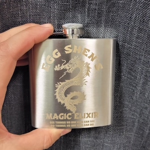 May include: A silver flask with a dragon design and the text "Egg Shen's Magic Elixir See things no one else can see Do things no one else can do".