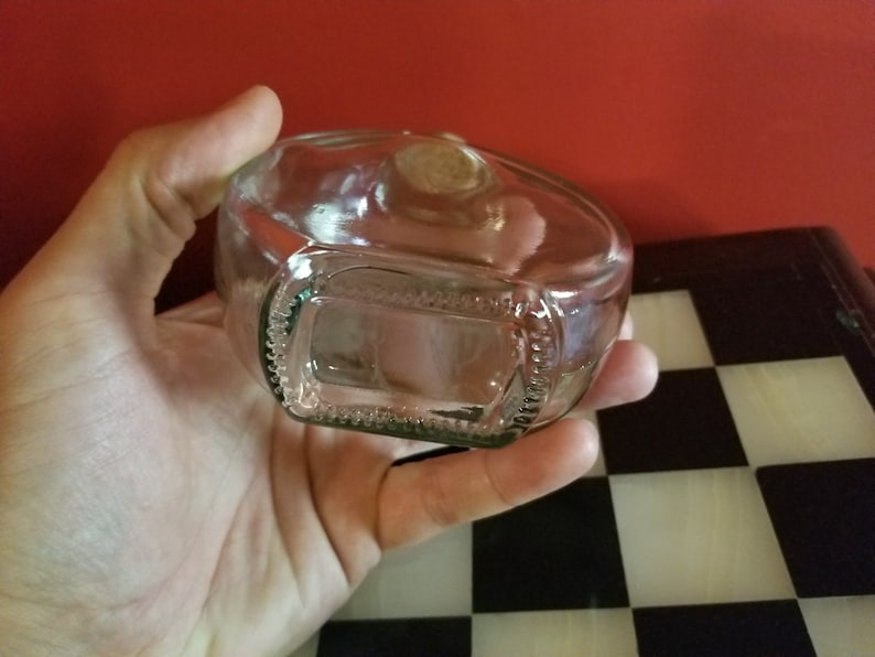 May include: A clear glass bottle with a textured bottom. The bottle is empty and has a cork stopper.