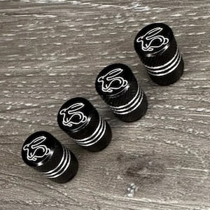 May include: Four black metal tyre valve stem caps with a white rabbit design.