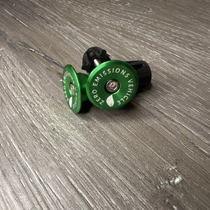 Puede incluir: Dos tapones de v&aacute;lvula de bicicleta verdes con tapas negras. El tap&oacute;n delantero tiene el texto "ZERO EMISSIONS VEHICLE" impreso.